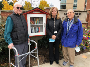 GHBC residents and art instructor stand next to little free library in front of GHBC