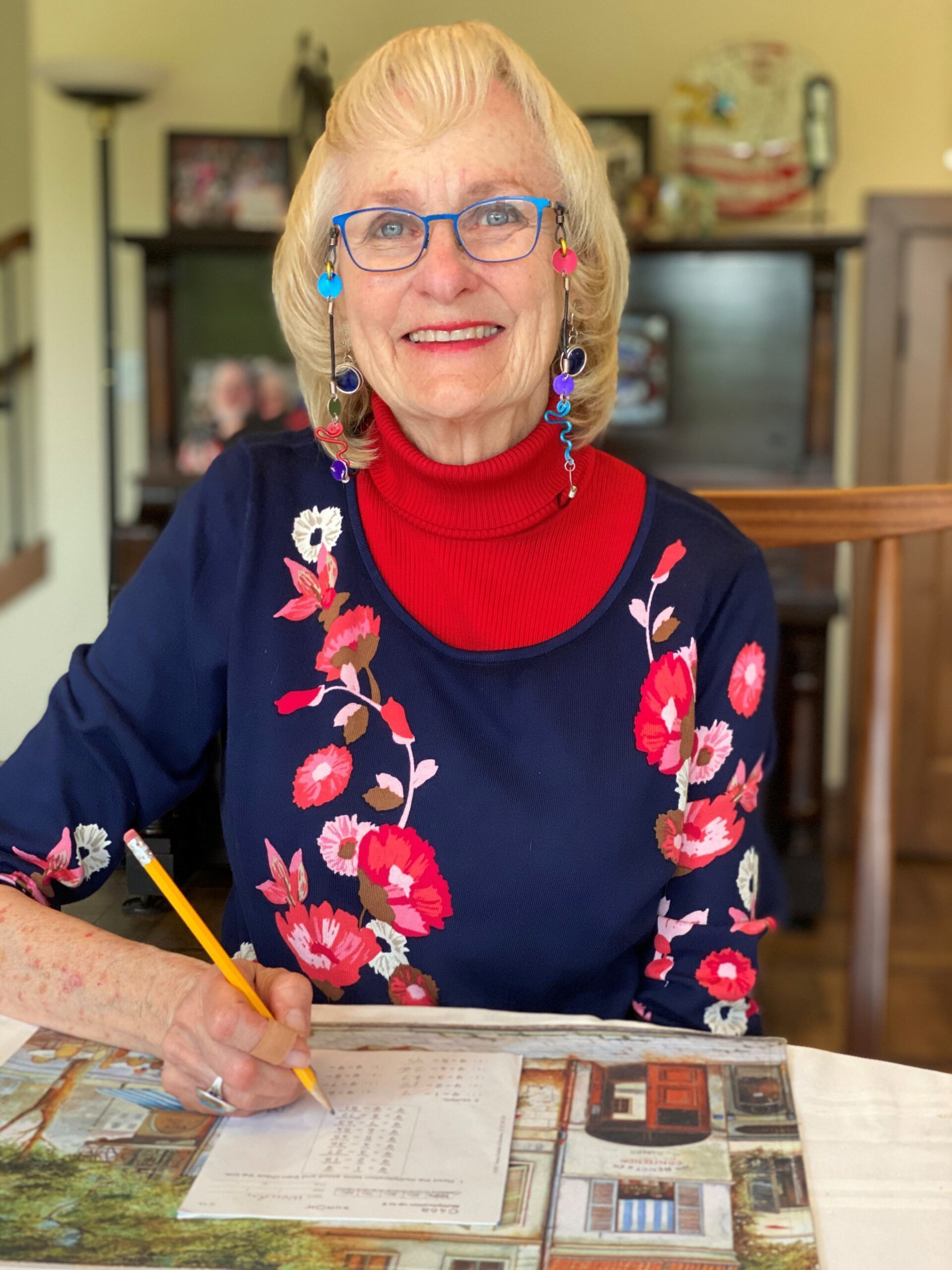 photo of an older woman in glasses. She is smiling as she works on a writing task